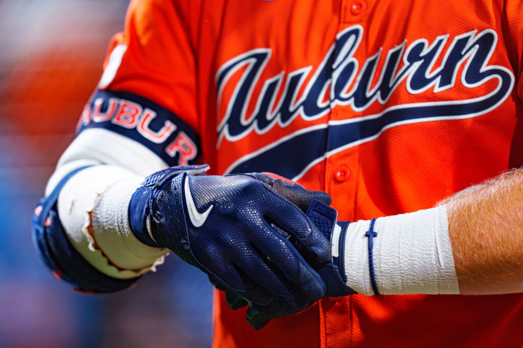 A baseball player in an Auburn uniform adjusts their navy blue glove while wearing a white wristband.